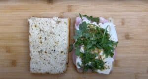 Open sandwich with ham, cream cheese, and arugula on a wooden board, ready to be assembled.